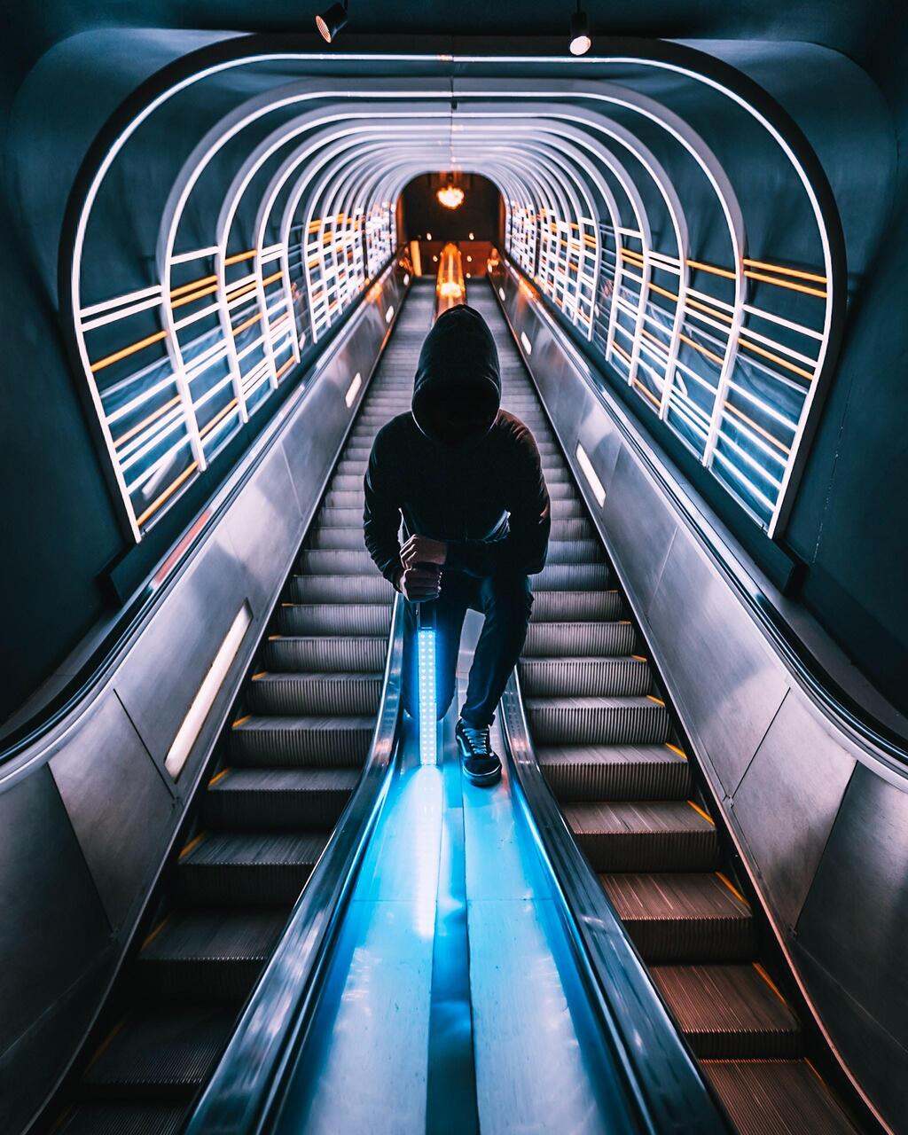 Persona encapuchada sobre escalera mecánica con un sable de luz en la mano.