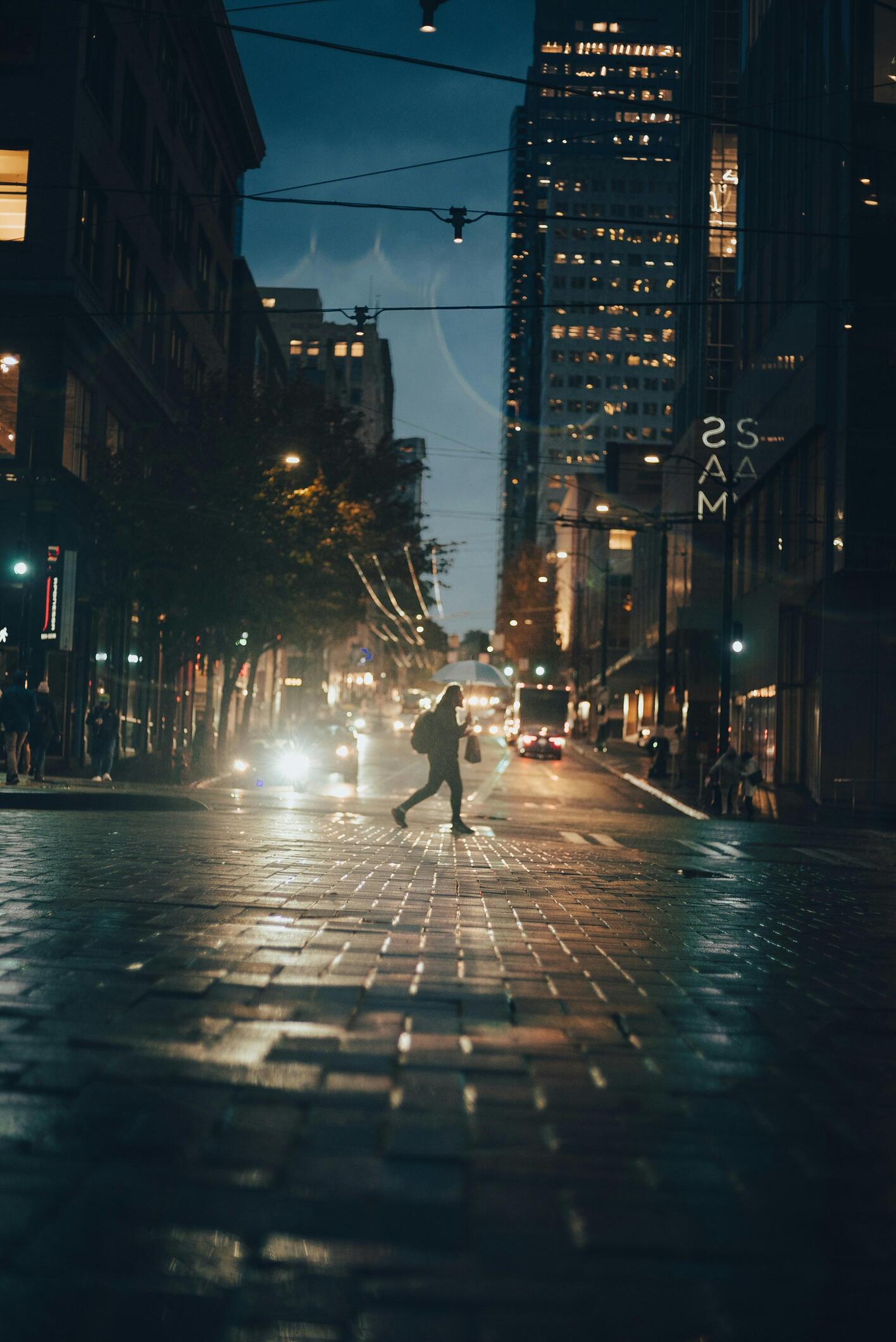 Persona cruzando la calle con las luces de los autos iluminándolo.